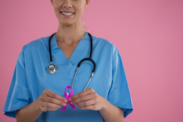Mid section of happy female doctor in scrubs showing Breast Cancer Awareness ribbon - Download Free Stock Photos Pikwizard.com