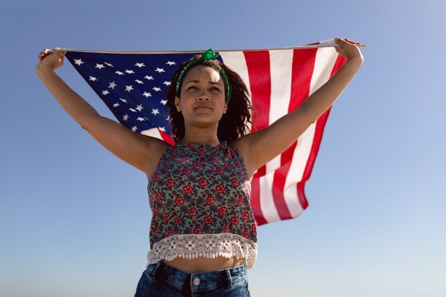 Low angle view of beautiful young Mixed-race woman waving american flag on beach in the sunshine