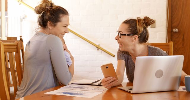 Two women collaborate excitedly at a table with a laptop, papers, and a smartphone. - Download Free Stock Photos Pikwizard.com
