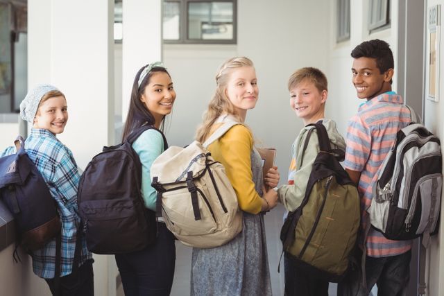Portrait of smiling students standing with notebook and school bag in corridor - Download Free Stock Photos Pikwizard.com