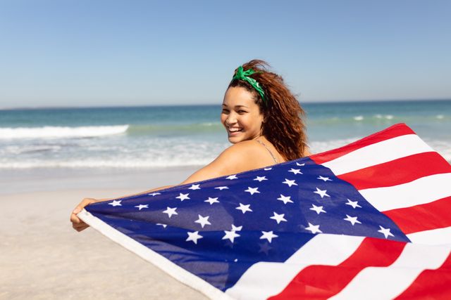 Rear view beautiful happy young Mixed-race woman waving american flag on beach in the sunshine