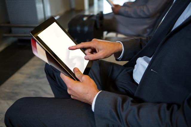 Mid-section of businessman using digital tablet while sitting at airport terminal