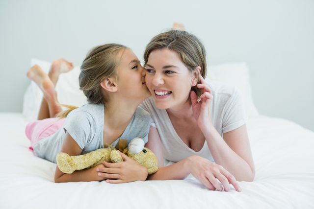 Adorable girl kissing her mother lying on a bed - Download Free Stock Photos Pikwizard.com
