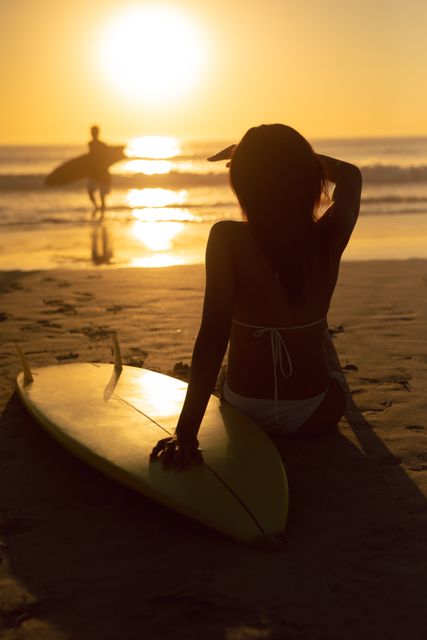 Rear view of woman with surfboard shielding her eyes while relaxing on the beach
