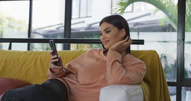 Image of happy biracial woman sitting on sofa and using smartphone. leisure, relax, spending free time with technology at home concept.