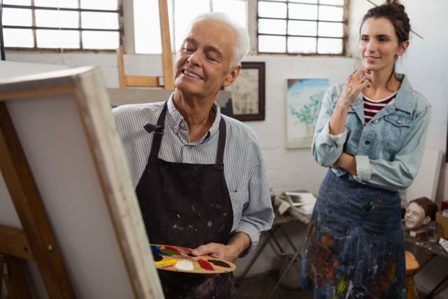 Woman watching while senior man painting on canvas - Download Free Stock Photos Pikwizard.com