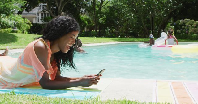 Happy african american woman relaxing at pool with family, using smartphone. family, togethernes, vacations and relax with technology concept.