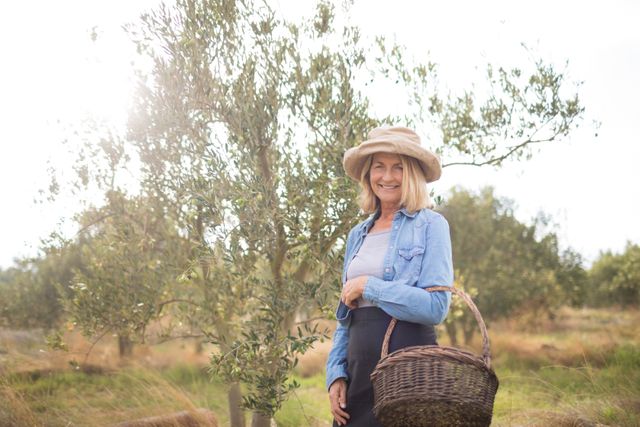 Portrait of happy of woman standing with basket in olive farm - Download Free Stock Photos Pikwizard.com