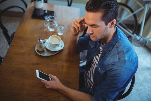 Man using mobile phone with cup of coffee on table in cafÃ©