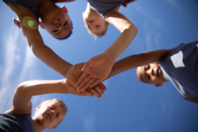 Directly below shot of multiracial elementary schoolboys stacking hands while standing against sky - Download Free Stock Photos Pikwizard.com