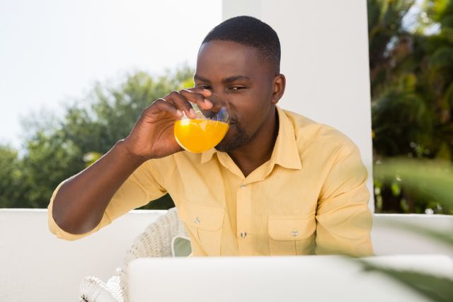 Young man drinking orange juice while looking at laptop - Download Free Stock Photos Pikwizard.com