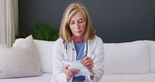 Portrait of caucasian senior female doctor taking notes while having a image call at home. distant communication and telemedicine consultation concept