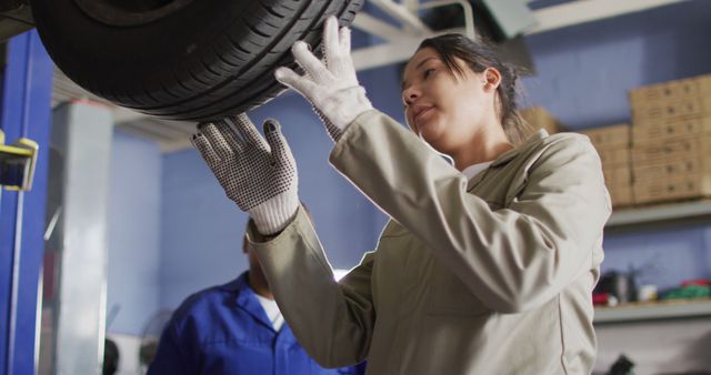 Image of two diverse female car mechanic talking and changing tyre. working in car repair shop and running small feminine business concept.