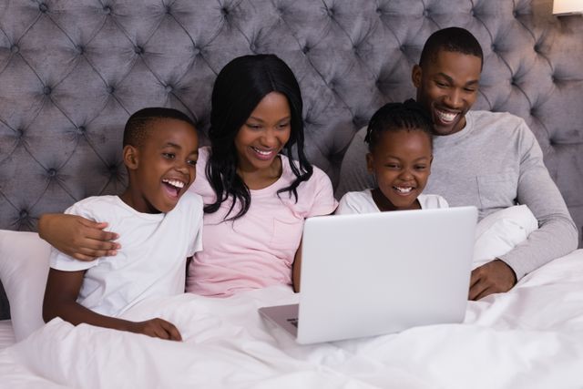 Happy family using laptop while sitting together on bed - Download Free Stock Photos Pikwizard.com