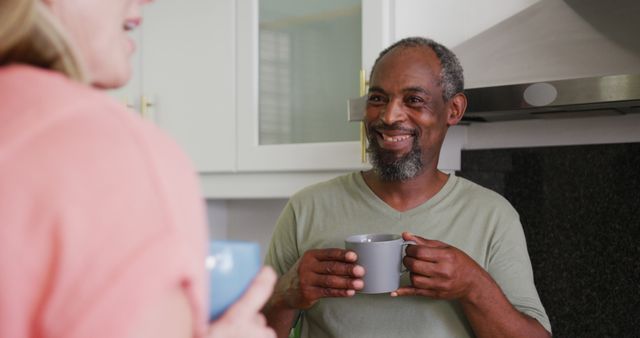 Over shoulder view of diverse senior couple drinking coffee smiling and talking in kitchen. staying at home in isolation during quarantine lockdown.