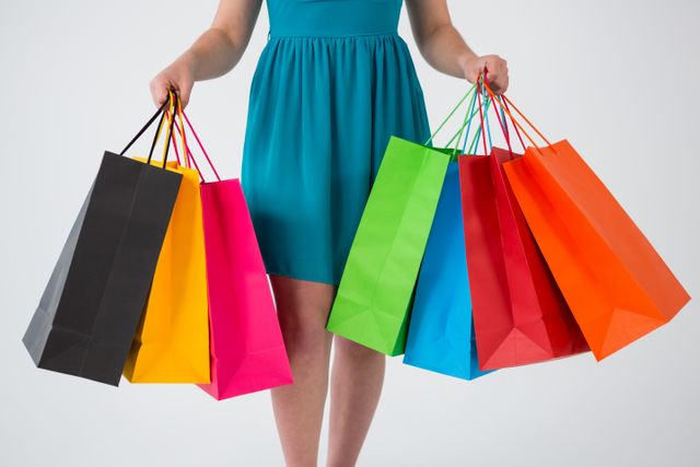 Mid section of woman carrying colorful shopping bags against white background