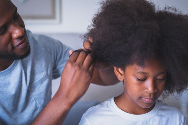 Smiling african american man styling his daughter's hair. staying at home in isolation during quarantine lockdown.