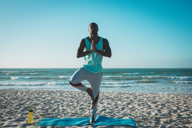 African american man exercising, practicing yoga, meditating on beach at sunset. healthy outdoor lifestyle fitness training.
