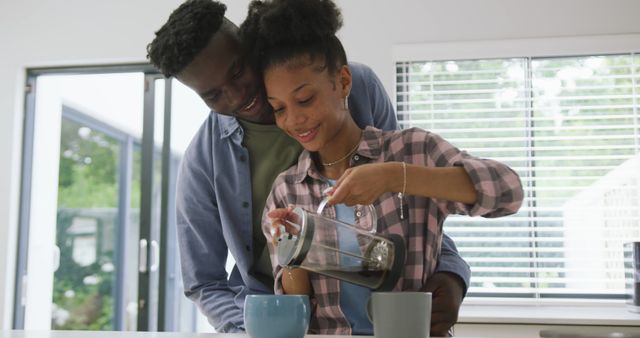 Image of happy african american couple preparing coffee and embracing at home. love, relationship, togetherness and spending quality time at home.