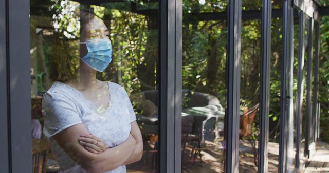 Asian woman wearing face mask and looking through window. at home in isolation during quarantine lockdown.