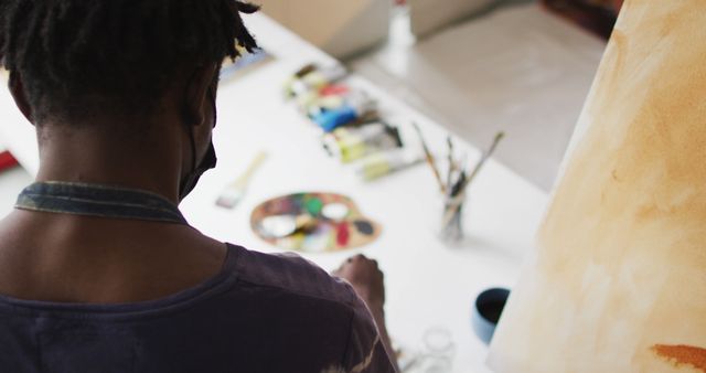 Rear view of african american male artist mixing colors in the palette with a brush at art studio. art, hobby and creative occupation concept
