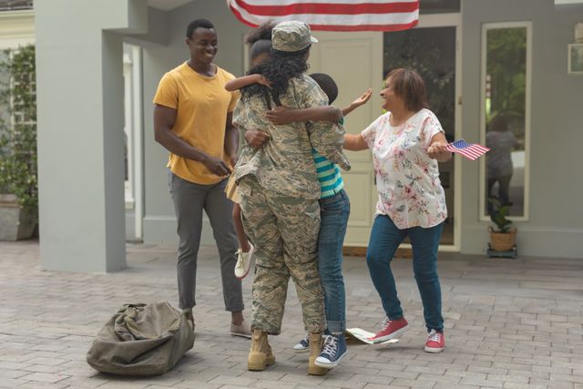 Happy family embracing african american female soldier outside house. unaltered, pride, military, armed forces, patriotism, homecoming, arrival, togetherness.