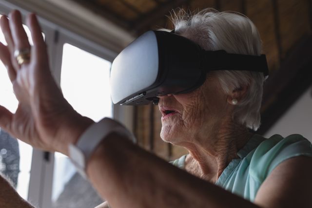 Close-up of a senior woman using virtual reality headset and raising her hand in living room at home