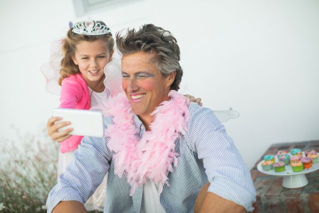 Cute daughter in fairy costume showing mobile phone to father - Download Free Stock Photos Pikwizard.com