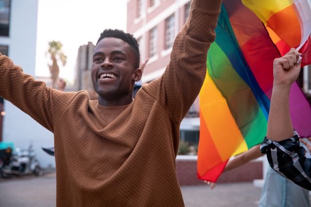 Smiling african american man holding rainbow flag during demonstration march - Download Free Stock Photos Pikwizard.com