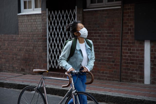 Young woman wearing face mask walking with her bicycle on the street - Download Free Stock Photos Pikwizard.com