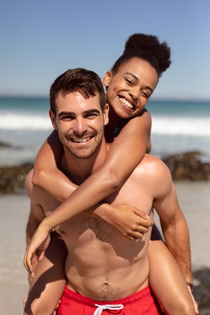 Man giving piggyback to woman on beach in the sunshine - Download Free Stock Photos Pikwizard.com