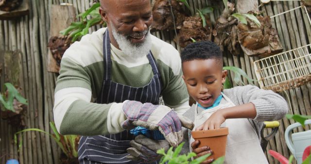 Happy senior african american man with his grandson potting up plants in garden. Spending time outdoors, working in garden nursery.