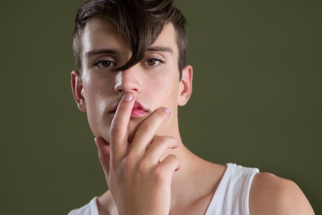 Androgynous man posing with finger on lips against green background