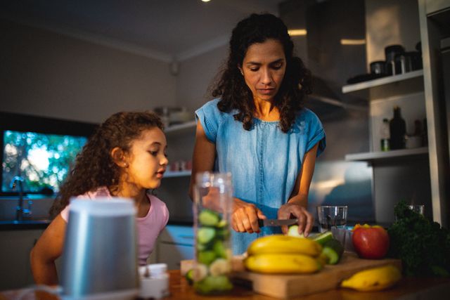 Mixed race mother and daughter preparing fruits for smoothie in kitchen. family spending time together at home.