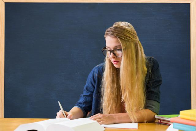 Female college student studying at table against blackboard - Download Free Stock Photos Pikwizard.com