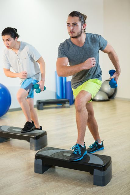 Two men doing step aerobic exercise with dumbbell on stepper - Download Free Stock Photos Pikwizard.com