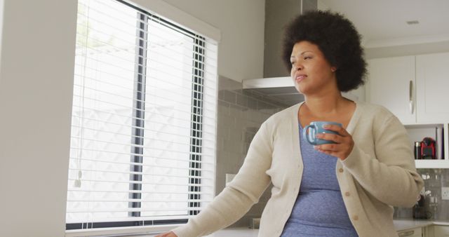 Image of happy plus size african american woman drinking coffee and using smartphone. lifestyle, leisure, spending free time at home with technology.