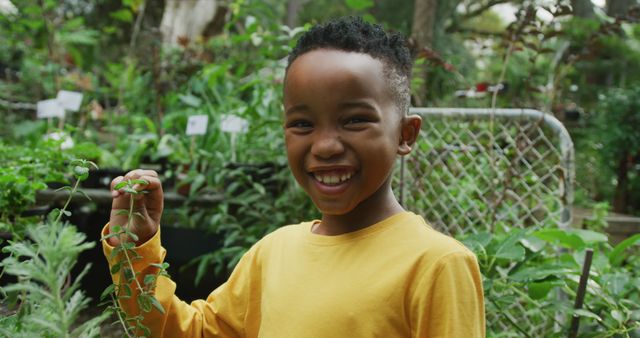Portrait of happy african american boy looking at plants and smiling in garden. Spending time outdoors, working in garden nursery.