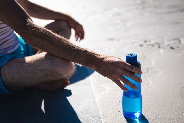 Low section of man sitting cross-legged holding water bottle on sunny day - Download Free Stock Photos Pikwizard.com
