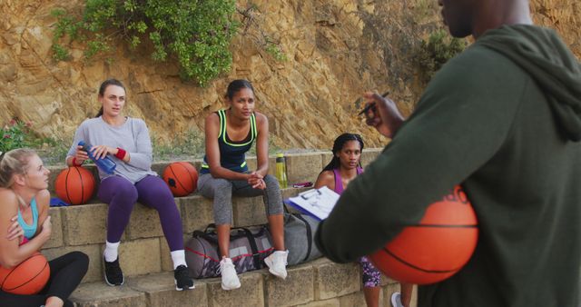 Diverse female basketball team and male coach discussing game tactics. basketball, sports training at an outdoor urban court.