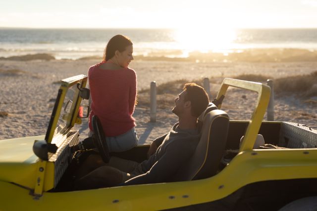 Caucasian couple sitting in beach buggy by the sea at sunset, talking. beach stop off on romantic summer holiday road trip.