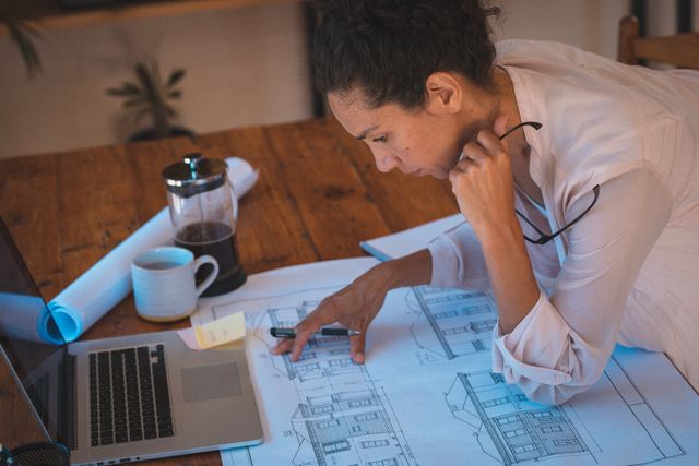Mixed race woman working at home studying architectural blueprints - Download Free Stock Photos Pikwizard.com