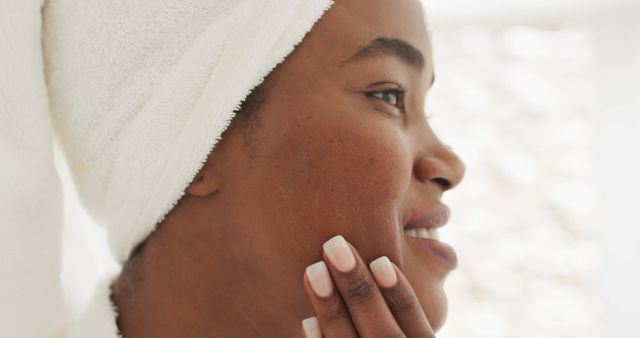 Image of happy african american woman in robe moisturizing face. beauty treatment and skin care routine concept.