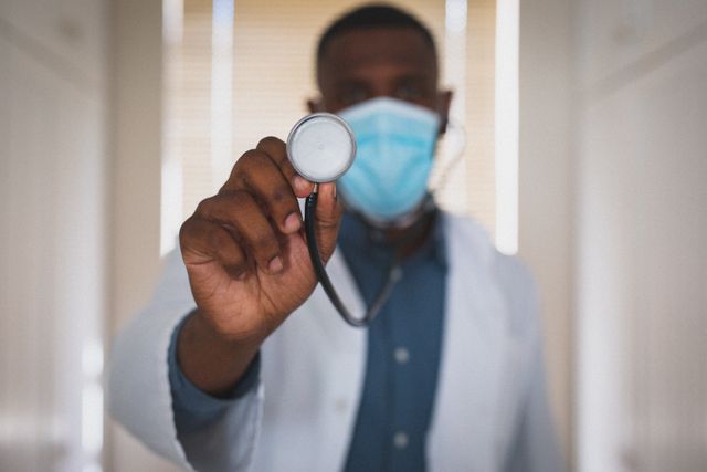 African american male doctor wearing face mask holding stethoscope to camera - Download Free Stock Photos Pikwizard.com