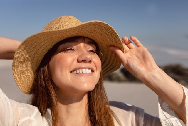 Beautiful woman in hat looking away on beach in the sunshine - Download Free Stock Photos Pikwizard.com