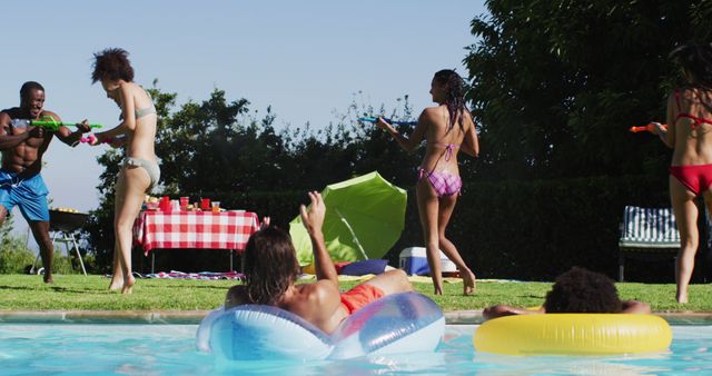 Mixed race woman having fun playing with water guns in swimming pool. hanging out and relaxing outdoors in summer.