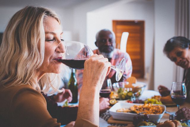 Senior caucasian woman drinking wine having dinner at home with diverse group of friends. retirement lifestyle, socialising with friends at home.