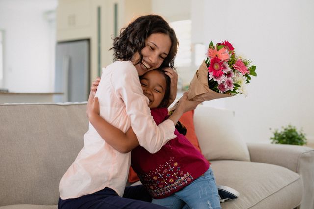 Happy hispanic mother holding flowers and hugging daughter on sofa - Download Free Stock Photos Pikwizard.com