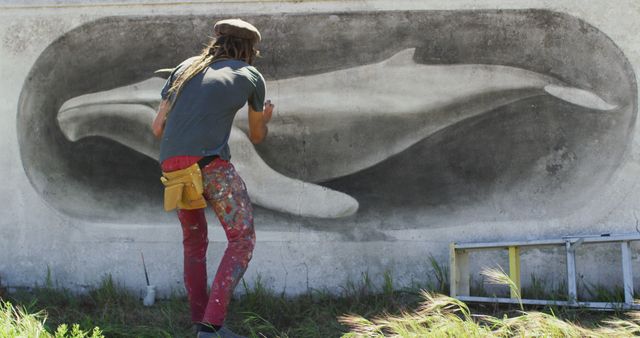 Image of rear view of caucasian male artist with dreadlocks painting whale mural on wall. Freedom, creativity, inclusivity and hobbies concept digitally generated image.