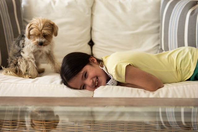 Little caucasian girl lying on the couch at home smiling beside her dog - Download Free Stock Photos Pikwizard.com